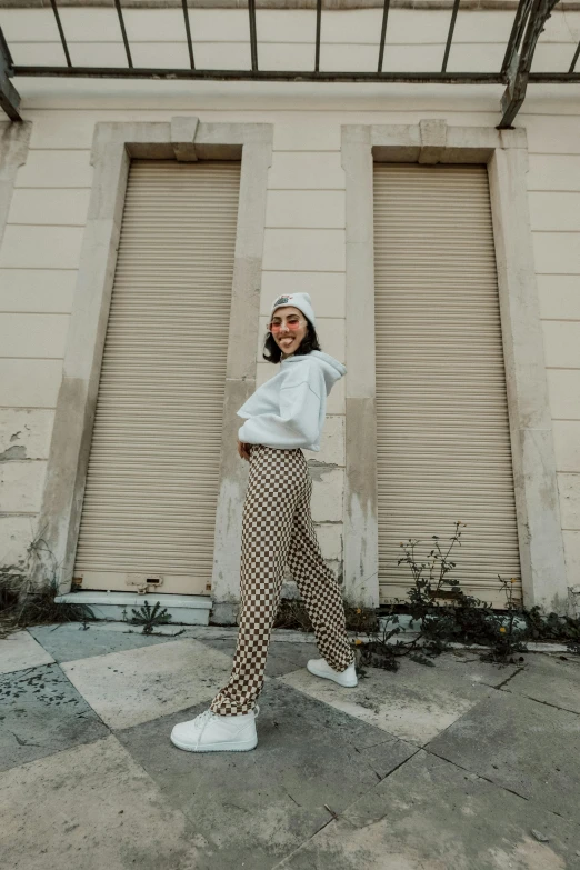 a woman standing in front of a building, trending on pexels, baggy pants, checkered floor, wearing a white sweater, she is happy