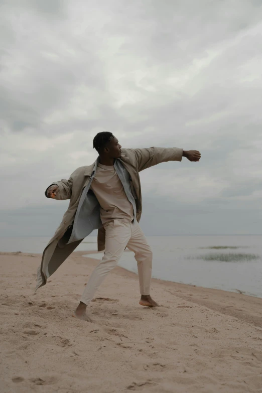 a man standing on top of a sandy beach, modern dance aesthetic, wearing a duster coat, battle pose, african man