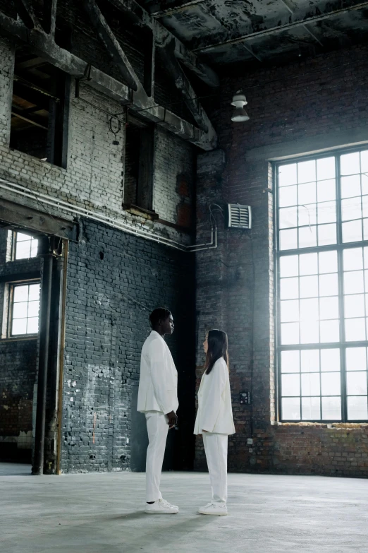a couple of people that are standing in a room, an album cover, unsplash, black arts movement, wearing white cloths, tall factory, exterior shot, ( ( theatrical ) )