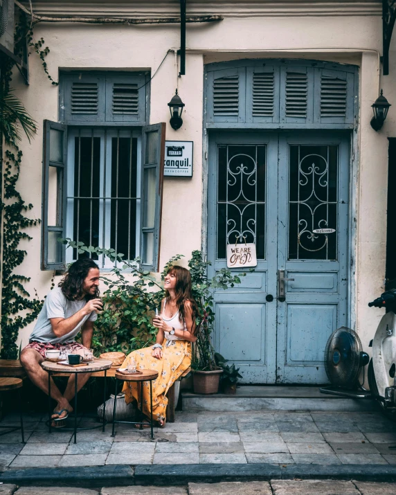 two people sitting on a bench in front of a building, pexels contest winner, greeks, eating outside, plants and patio, in doors