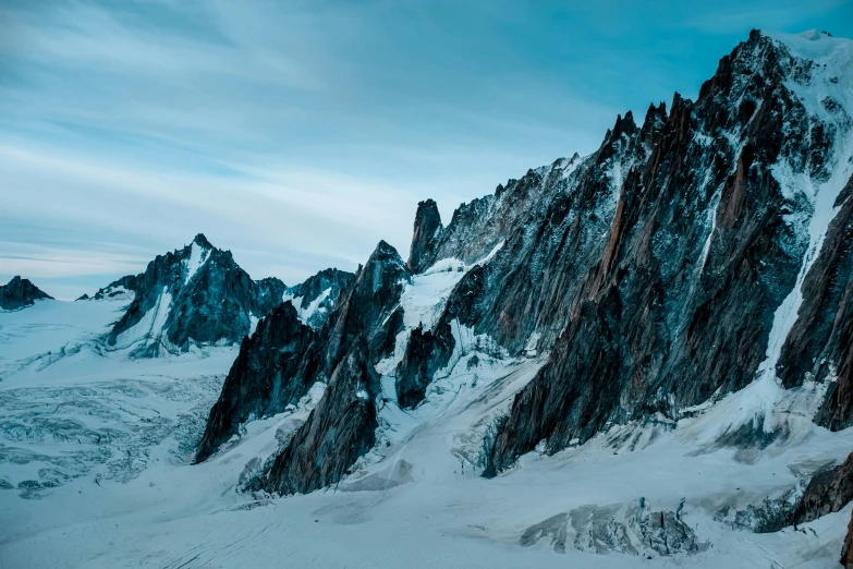 a man standing on top of a snow covered mountain, by Pierre Mion, pexels contest winner, visual art, tall stone spires, “ aerial view of a mountain, rugged face, photography shot at blue hour