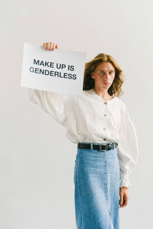 a woman holding a sign that says make up is genderless, an album cover, by Ellen Gallagher, trending on unsplash, tilda swinton, white shirt and grey skirt, angela sarafyan, nonbinary model