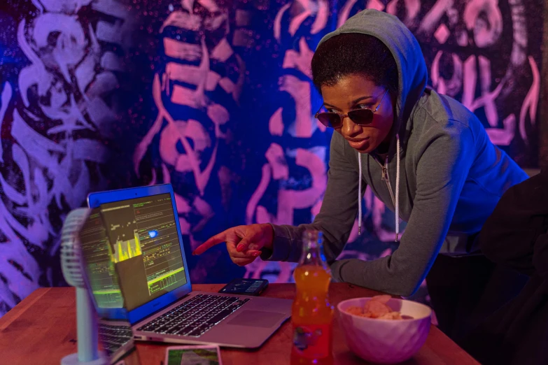 a woman sitting at a table in front of a laptop, graffiti, ashteroth, at a rave, hacking, trending photo