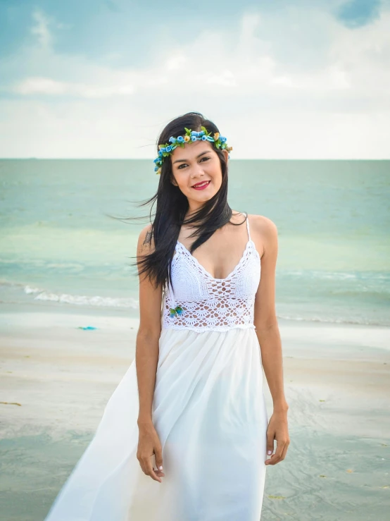 a woman in a white dress standing on a beach, by Robbie Trevino, pexels contest winner, wearing a floral crown, gemma chan beautiful girl, graduation photo, wearing white camisole