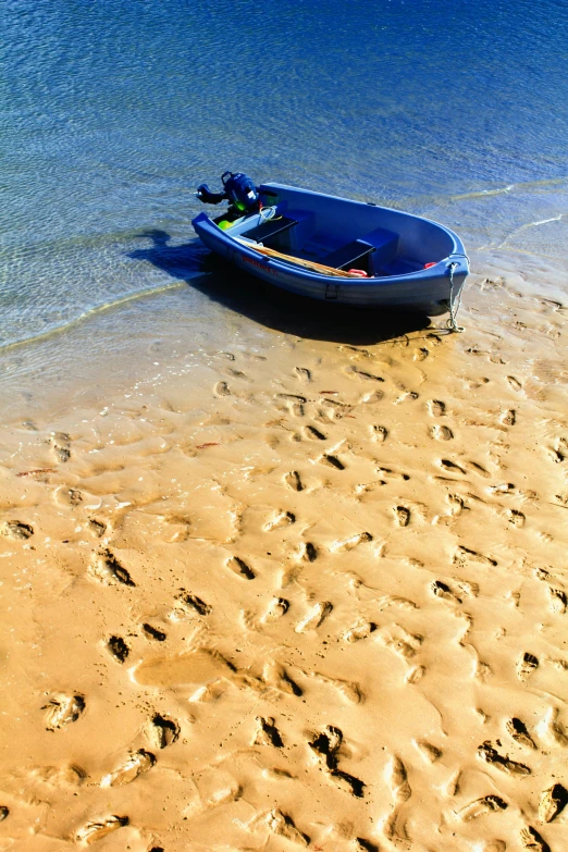 a blue boat sitting on top of a sandy beach, footprints in the sand, dingy, beach on the outer rim, cast