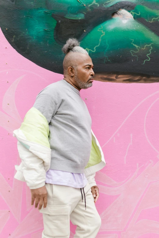 a man standing in front of a wall with a painting on it, inspired by Barkley Hendricks, trending on unsplash, grey hair, style of takashi murakami, patron saint of 🛸🌈👩🏾, pastel clothing