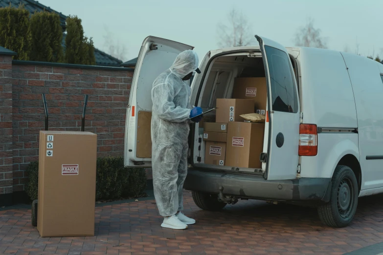 a man in a protective suit loading boxes into a van, pexels contest winner, brown, avatar image, ecommerce photograph, grey