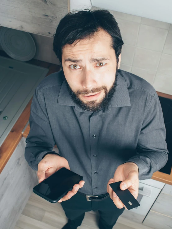 a man standing in a kitchen holding two cell phones, trending on reddit, renaissance, looking down on the camera, square, high quality photo, frustrated expression