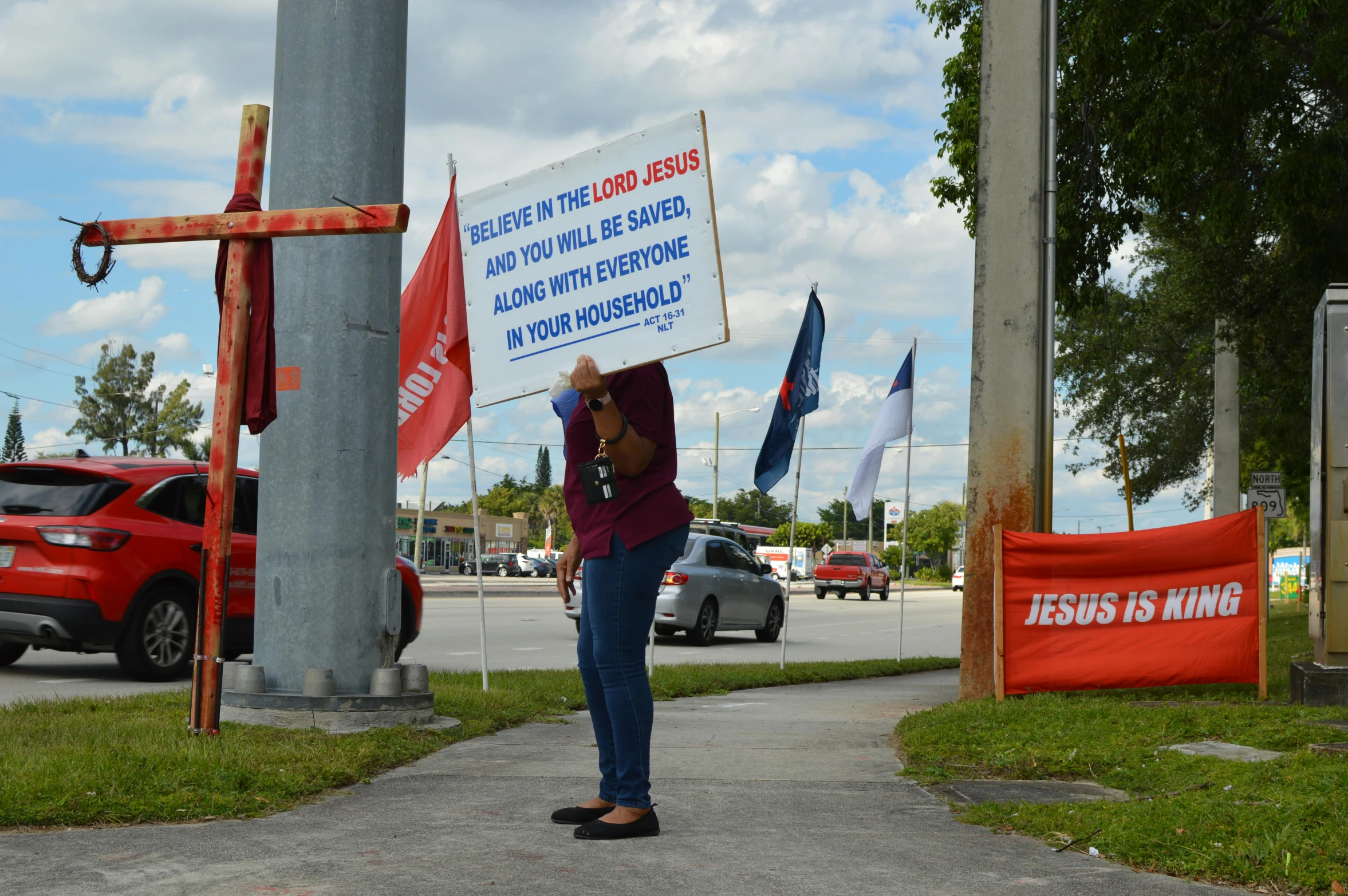 a woman standing on a sidewalk holding a sign, a photo, by Robbie Trevino, florida man, jesus, square, hongbsws