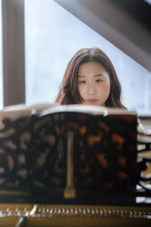 a woman sitting at a piano in front of a window, an album cover, by Kim Eung-hwan, pexels contest winner, li bingbing, reading a book, square, concert photo