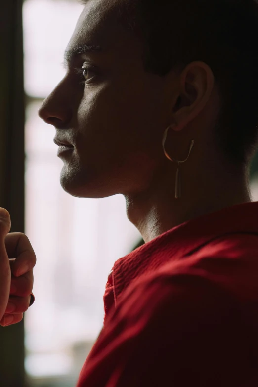 a close up of a person holding a cell phone, inspired by Nan Goldin, earring, light stubble with red shirt, looking out a window, an epic non - binary model