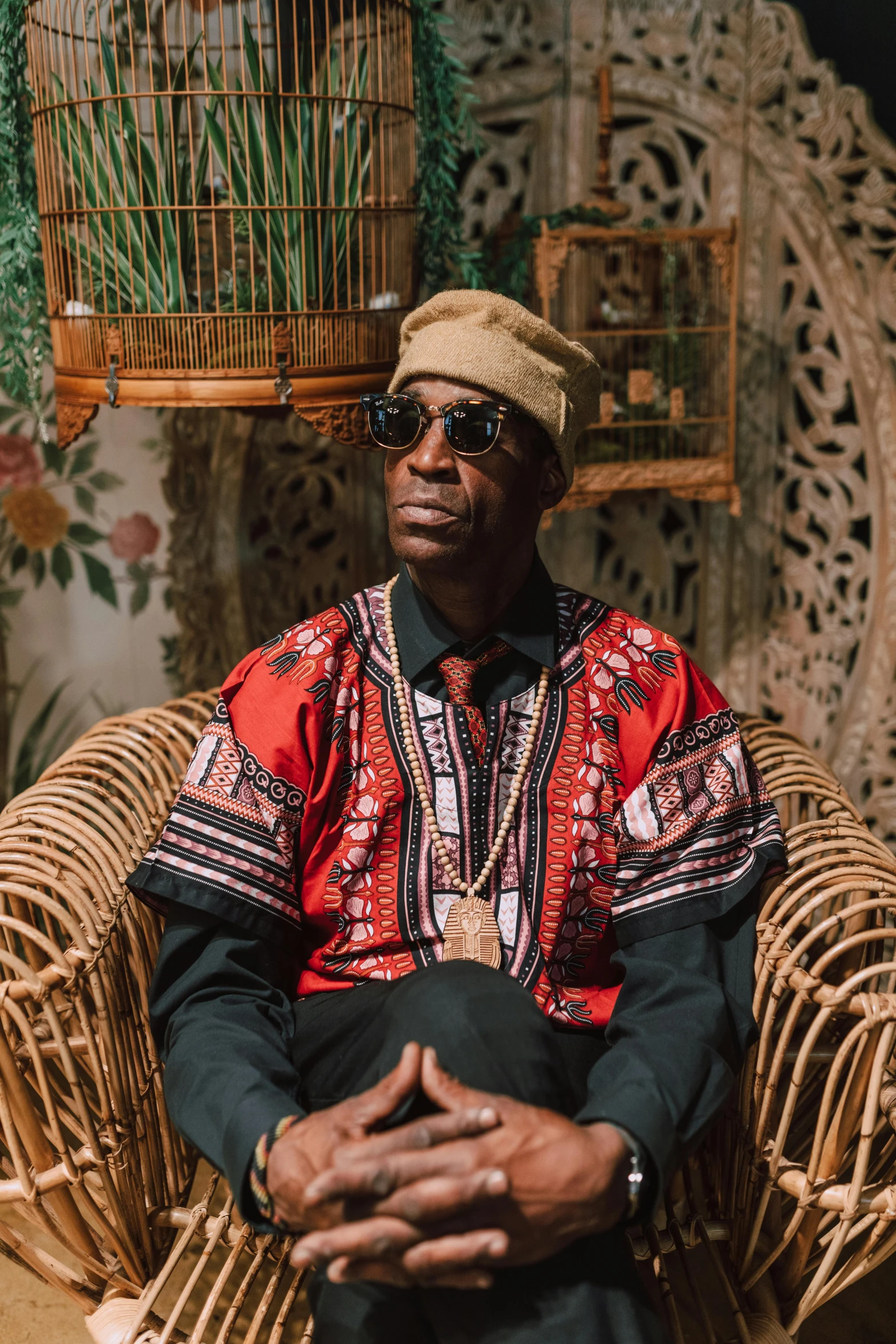 a man sitting in a chair next to a bird cage, an album cover, inspired by Barthélemy Menn, unsplash, afrofuturism, patterned clothing, rastafarian, blind brown man, a wooden