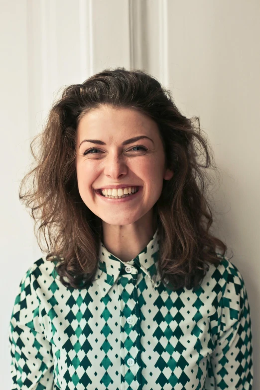 a woman standing in front of a white wall, dark short curly hair smiling, marina federovna, multiple stories, patterned