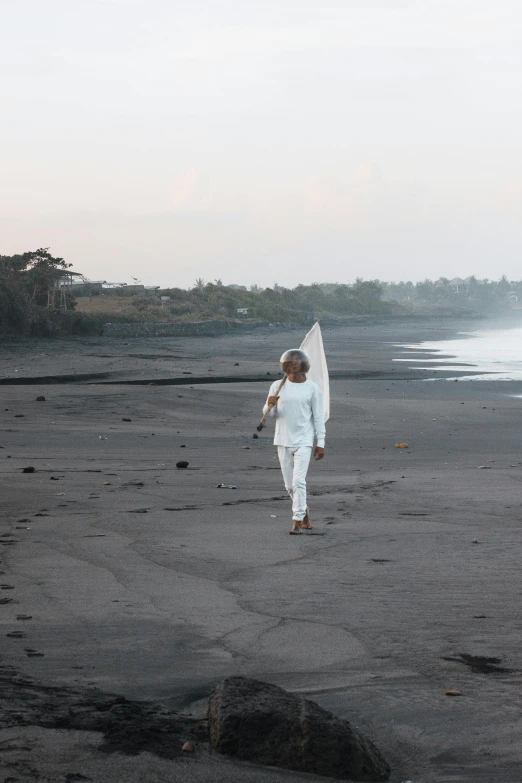 a person walking on a beach with a surfboard, inspired by Barthélemy Menn, happening, black volcano afar, white sarong, evening time, on location