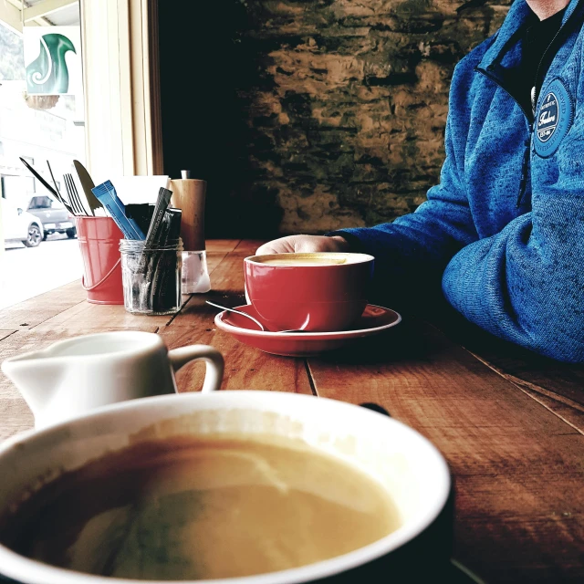 a woman sitting at a table with a cup of coffee, a photo, by Lee Loughridge, instagram picture, soup, thumbnail, low quality grainy