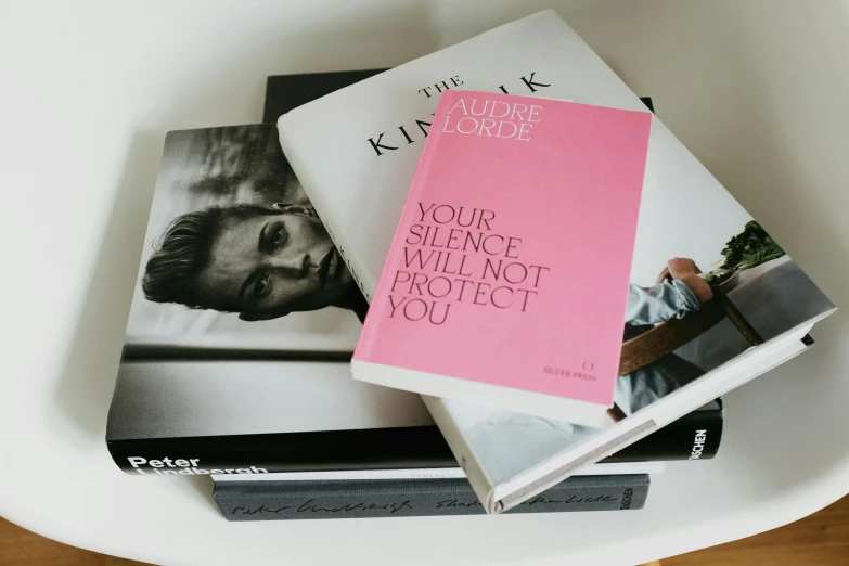 a stack of books sitting on top of a white table, a black and white photo, private press, pink accents, fashion magazine cover, informative texts, protective