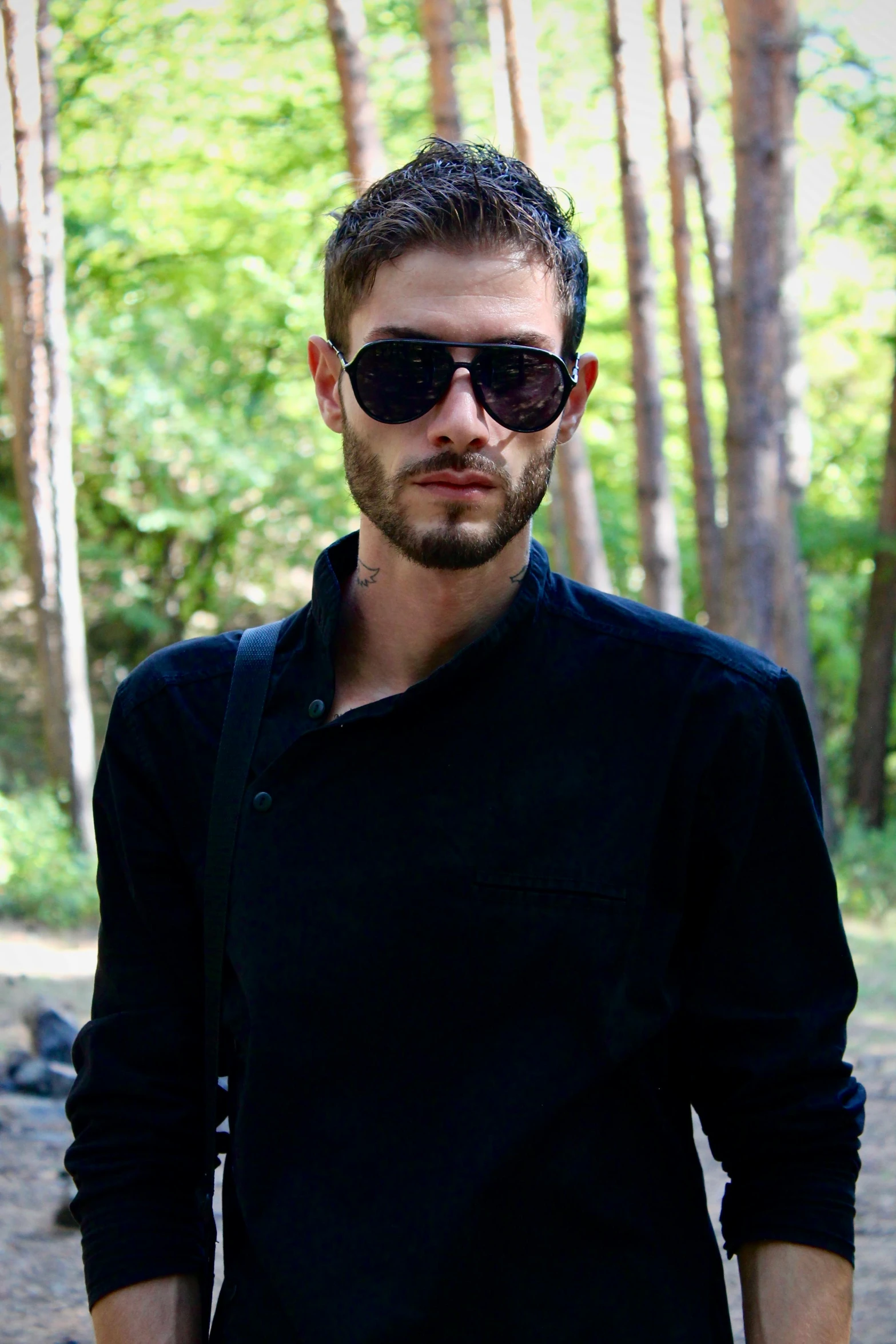 a man standing in the woods with his hands in his pockets, spiked collar sunglasses, with a beard and a black shirt, stjepan sejic, 2 3 years old