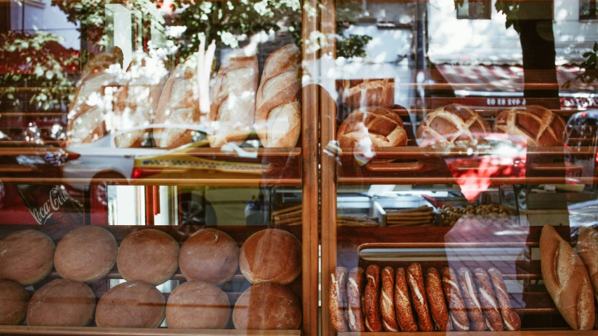 a display case filled with lots of different types of bread, a photo, by Julia Pishtar, pexels, art nouveau, seen through a window, holding a baguette, al fresco, thumbnail