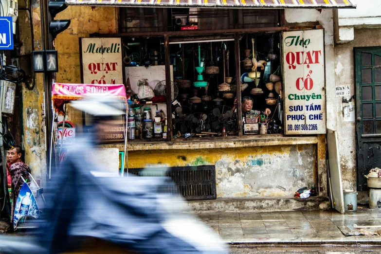 a man riding a motorcycle down a street past a store, inspired by Steve McCurry, pexels contest winner, phuoc quan, a quaint, panoramic shot, a messy