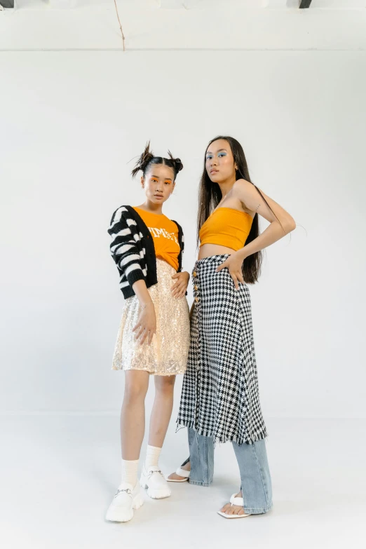 a couple of women standing next to each other, inspired by Wang Duo, unsplash, kitsch movement, black and orange, plaid skirt, bella poarch, wearing a crop top