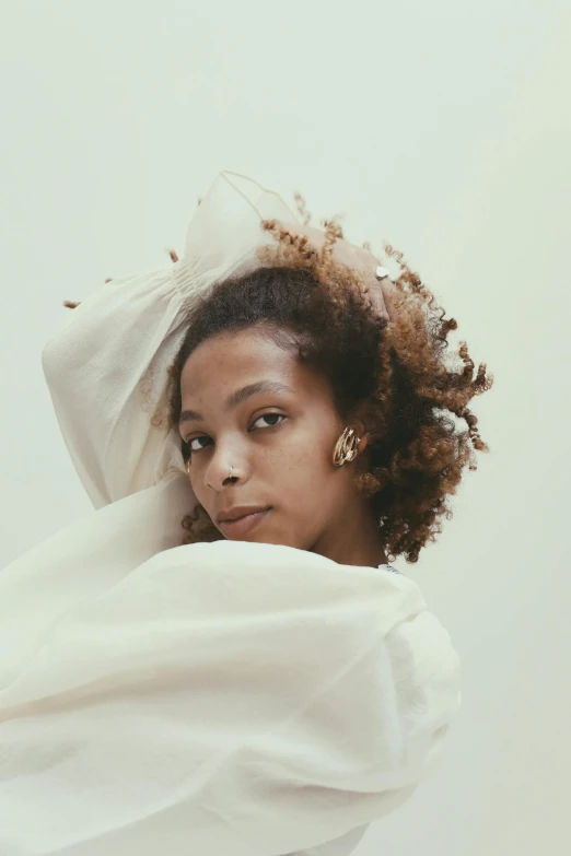 a woman standing in front of a white wall, an album cover, inspired by Gordon Parks, renaissance, flowing golden scarf, wearing white robes, natural hair, wrapped in cables and flowers