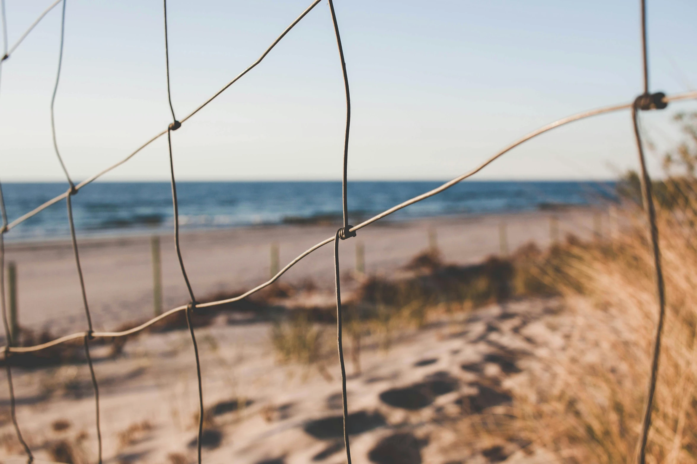 a view of a beach through a fence, by Niko Henrichon, unsplash, conceptual art, steel wire, late afternoon, slightly tanned, instagram post