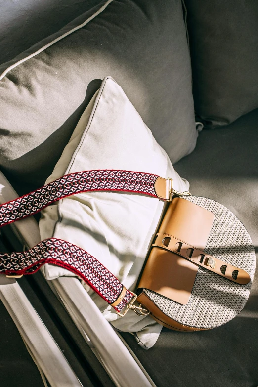 a purse sitting on top of a couch next to a pillow, inspired by Eugène Brands, trending on unsplash, happening, intricate leather suspenders, crimson and white color scheme, white belt, geometry
