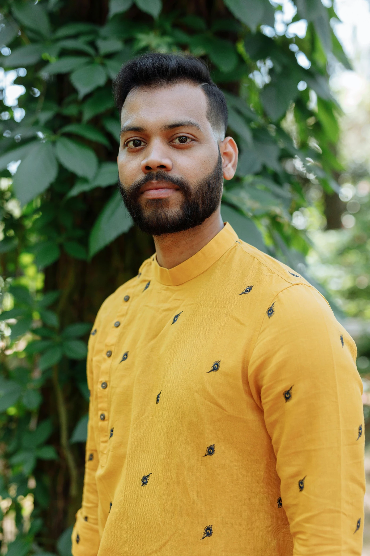 a man standing in front of a tree, wearing yellow floral blouse, a portrait of rahul kohli, assamese, wearing a linen shirt