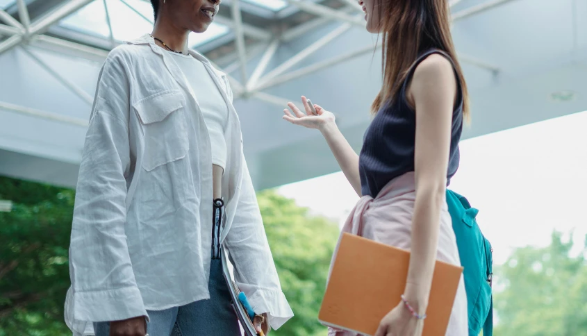 a man and a woman standing next to each other, trending on pexels, academic clothing, talking, woman holding another woman, fiona staples and kinu nishimura