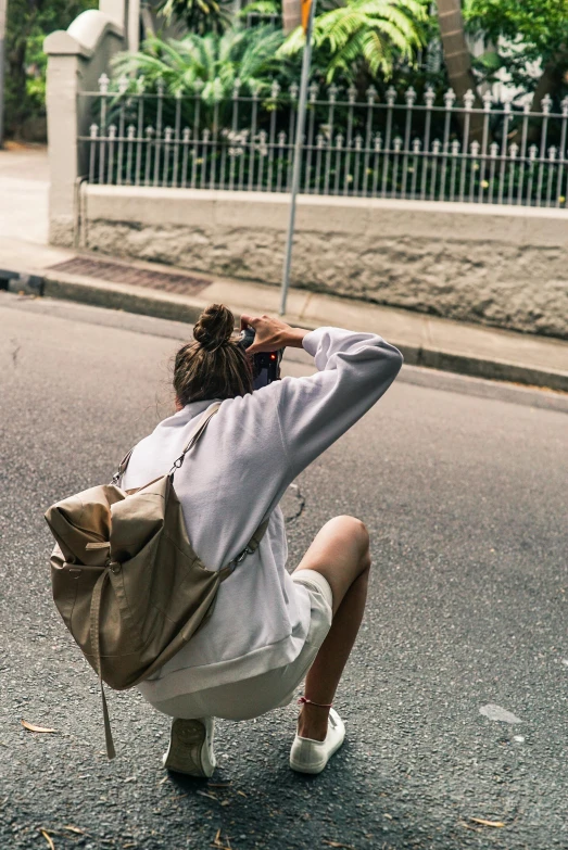 a woman kneeling on the side of the road holding an umbrella, by Nina Hamnett, trending on unsplash, beige hoodie, holding a gold bag, man sitting facing away, bra and shorts streetwear