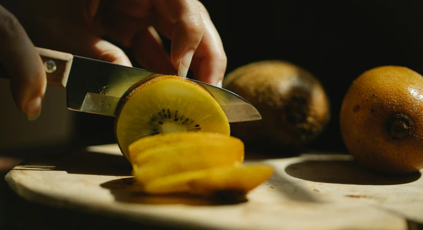 a person cutting a kiwi on a cutting board, a still life, by Niko Henrichon, pexels contest winner, 🦩🪐🐞👩🏻🦳, brown, dimly - lit, mango