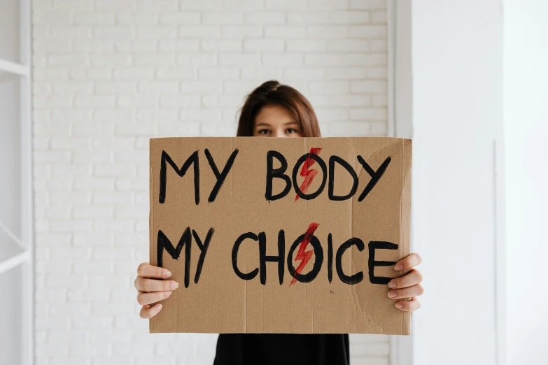 a woman holding a sign that says my body is my choice, trending on pexels, organ harvesting, profile image, cardboard, third trimester