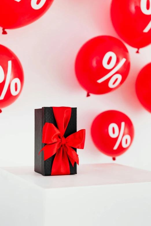 a black gift box sitting on top of a table surrounded by red balloons, by Julia Pishtar, 7 0 % ocean, thick bow, product shot, mathematical