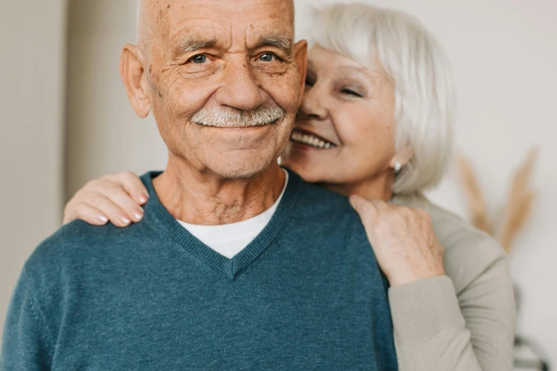 an older man and woman hugging each other, pexels contest winner, photorealism, smiling and looking directly, background image, closeup of arms, scientific photo