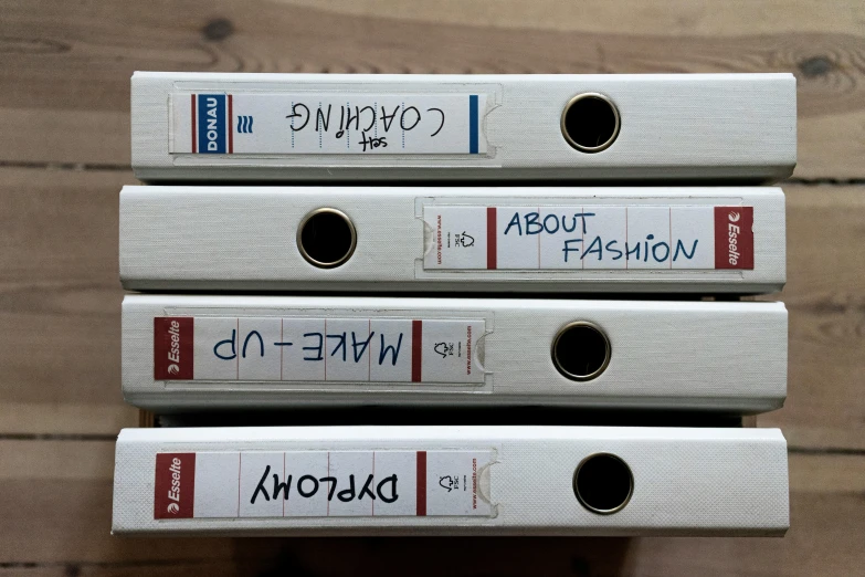 a stack of white binders sitting on top of a wooden table, an album cover, unsplash, art informel, catwalk, handwriting title on the left, wearing fashion clothing, onscreen info and labels