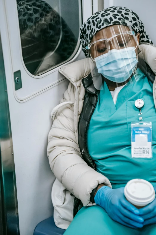 a woman wearing a face mask sitting on a train, a picture, surgical gown and scrubs on, nyc, african american woman, nurse costume