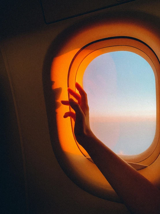 a person's hand reaching out of an airplane window, pexels contest winner, 🚿🗝📝, lofi girl aesthetic, yellow and orange color scheme, lights are on in the windows