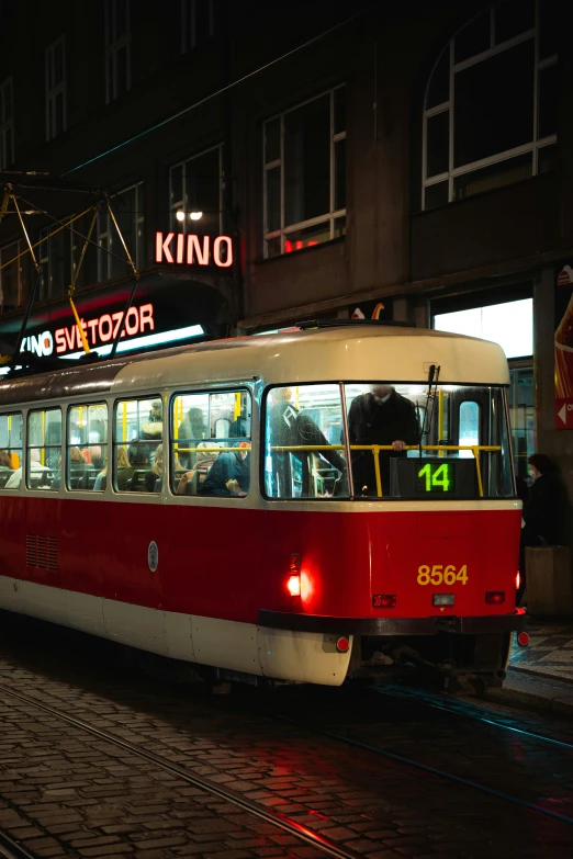 a red and white train on a city street, inspired by Stanisław Tondos, viennese actionism, red neon lights inside it, kino, brown, prague