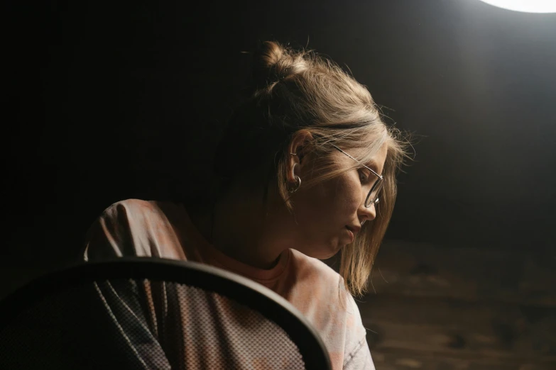 a woman sitting in a chair looking at her cell phone, inspired by Elsa Bleda, trending on pexels, somber lighting, girl wearing round glasses, dusty light, profile image