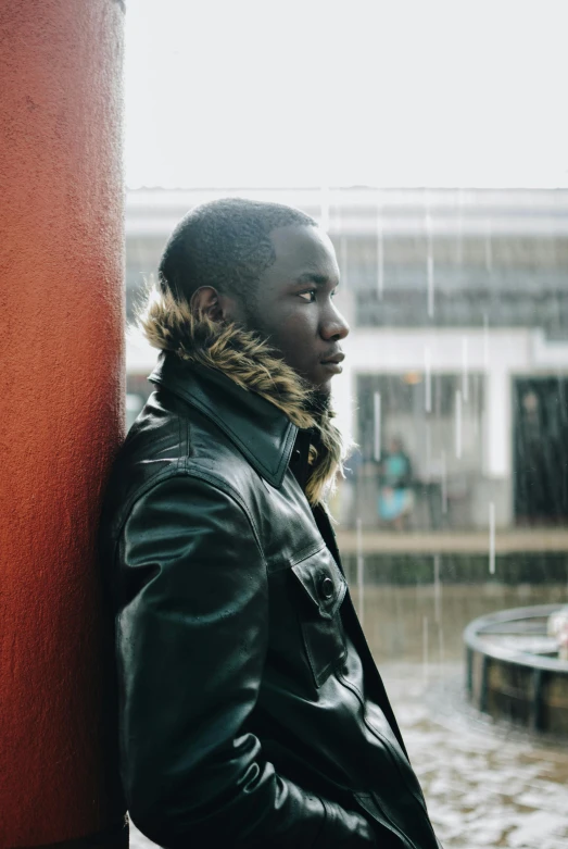 a man leaning against a red wall in the rain, an album cover, by Terrell James, trending on pexels, wearing a turtleneck and jacket, ( ( dark skin ) ), distant thoughtful look, sittin