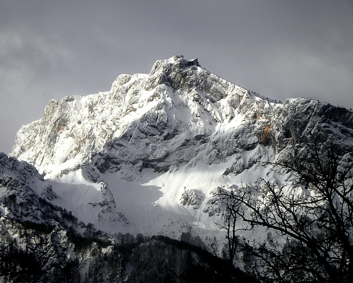 a snow covered mountain with trees in the foreground, by Cedric Peyravernay, pexels contest winner, sharp cliffs, grey, 2000s photo, wikimedia