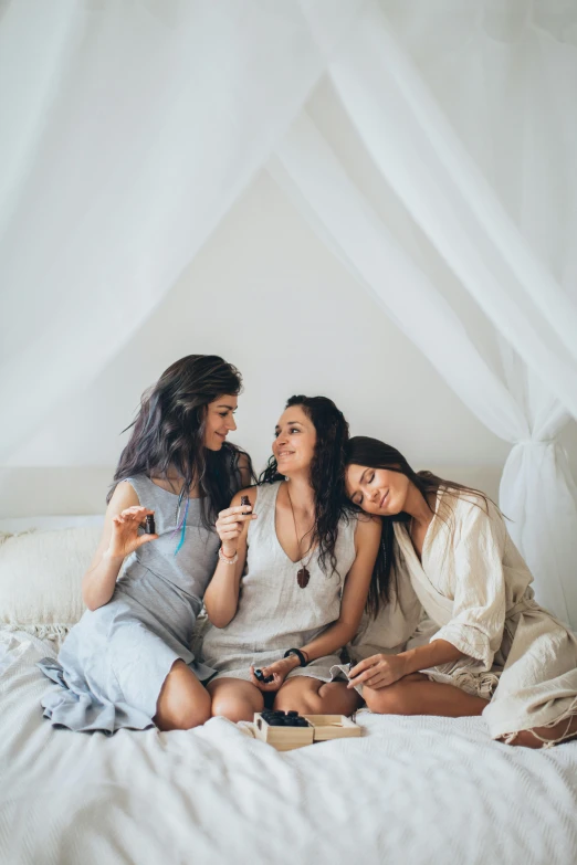 a group of women sitting on top of a bed, trending on unsplash, romanticism, three women, brunette, white hue, snapchat photo