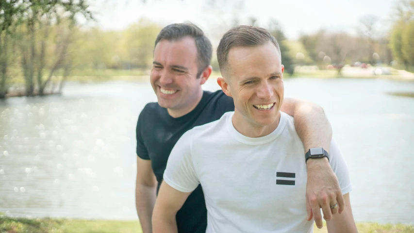 a couple of men standing next to each other, profile image, with a park in the background, both laughing, avatar image