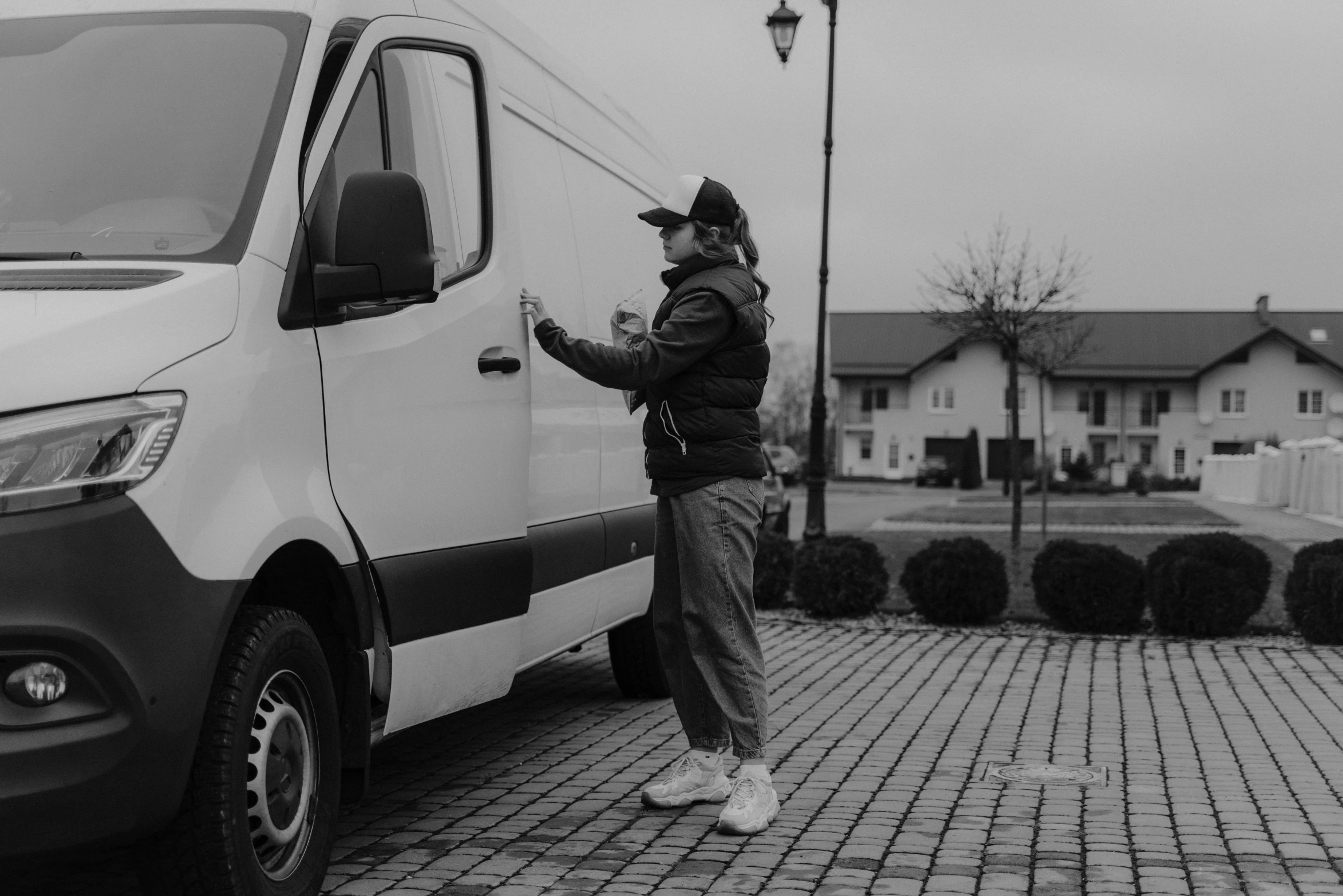 a man standing in front of a white van, a black and white photo, by Emma Andijewska, pexels contest winner, delivering mail, avatar image, young female, maintenance photo