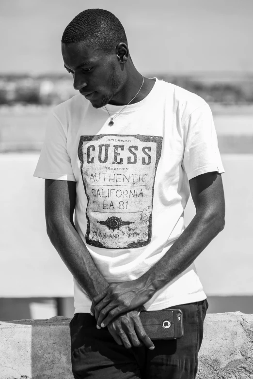 a black and white photo of a man leaning against a wall, inspired by Theo Constanté, happening, wearing a t-shirt, tupac, los angeles 2 0 1 5, jeans and t shirt