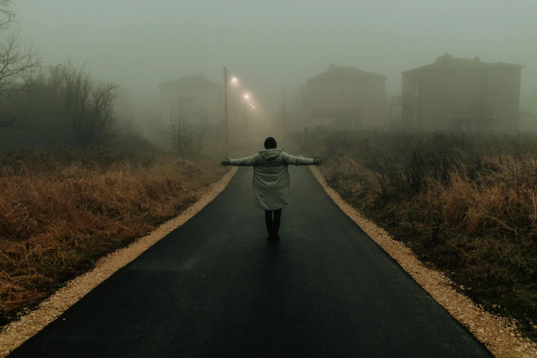 a person walking down a road on a foggy day, an album cover, by Lucia Peka, pexels contest winner, magical realism, arms spread wide, abandoned streets, ignant, movie still 8 k