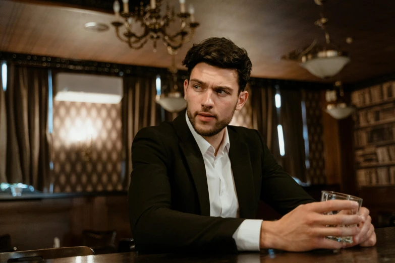 a man sitting at a bar with a glass in his hand, a portrait, pexels contest winner, wearing causal black suits, young greek man, thumbnail, serious look