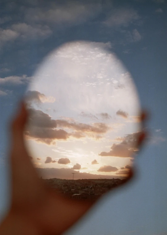 a person holding up a mirror with a sunset in the background, inspired by Anna Füssli, translucent eggs, smooth oval head, clouds visible, brain visible