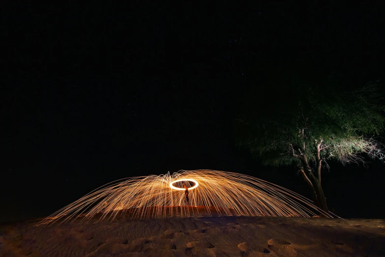 a man standing on top of a sandy beach next to a tree, unsplash contest winner, land art, sparklers, in a circle, night time australian outback, lighting on concrete