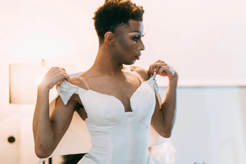 a woman in a white dress standing in front of a mirror, androgynous male, wearing corset, in style of tyler mitchell, pictured from the shoulders up